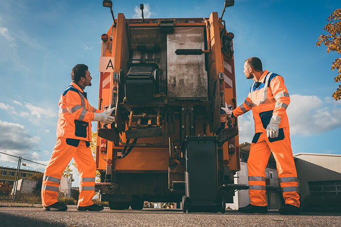 Das Foto zeigt zwei Müllmänner auf der Rückseite eines Müllwagens.